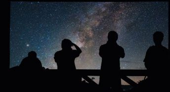 Four people stargazing silhouetted against the milky way