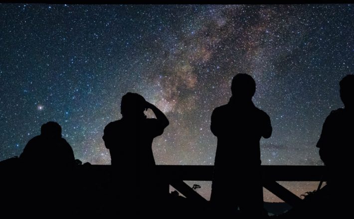 Four people stargazing silhouetted against the milky way