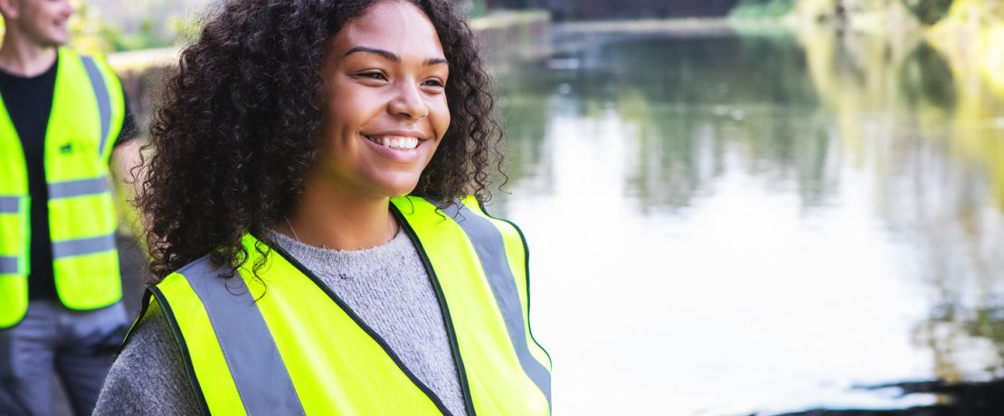 Smiling woman looking out across river wearing CPRE hi vis vest with man in background