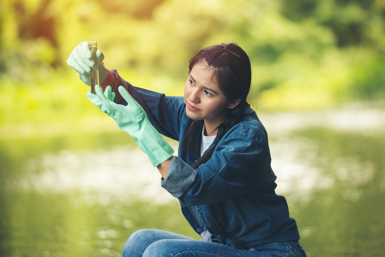 Woman holding a glass tube of river water as she checks the quality of the water